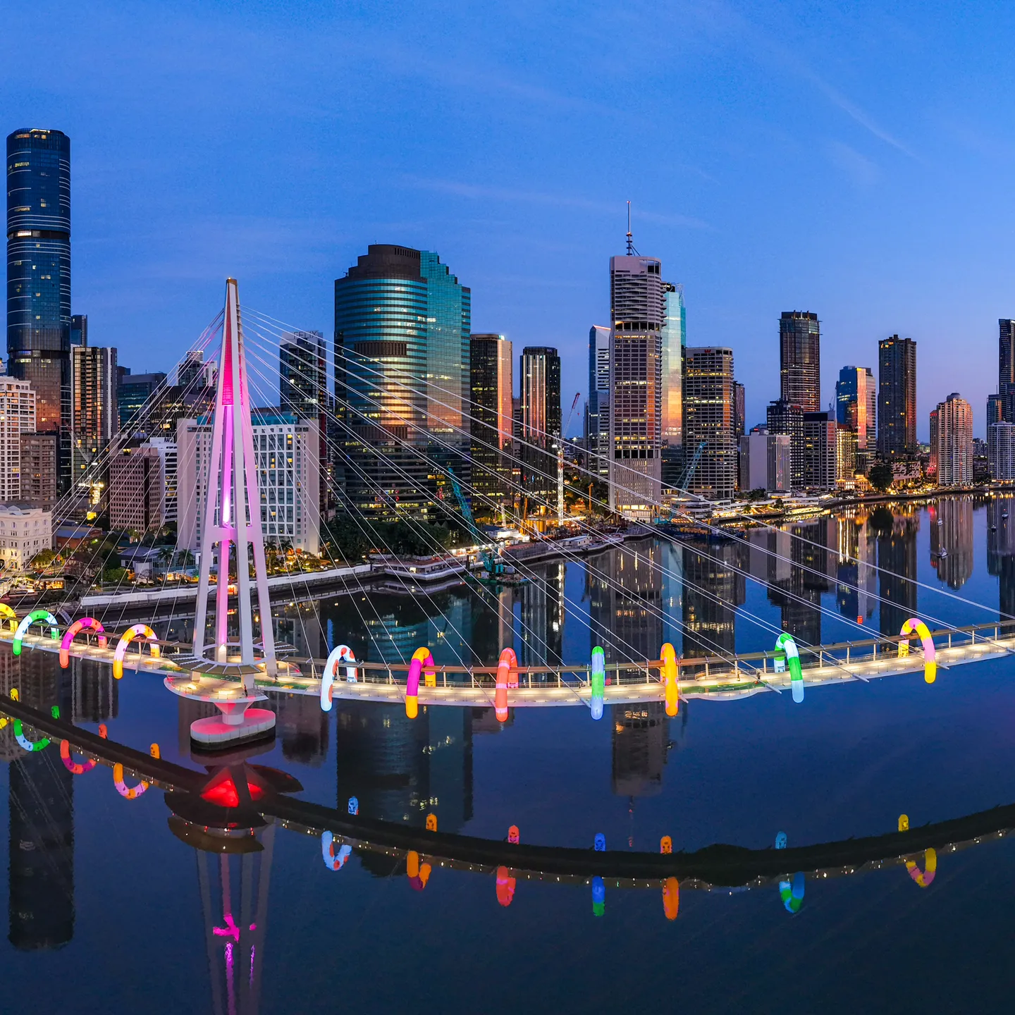 An aerial view of Brisbane city at dawn with Kangaroo Point Bridge lit up with rainbow arches of ANZ's Walk This Way by Craig Karl. 