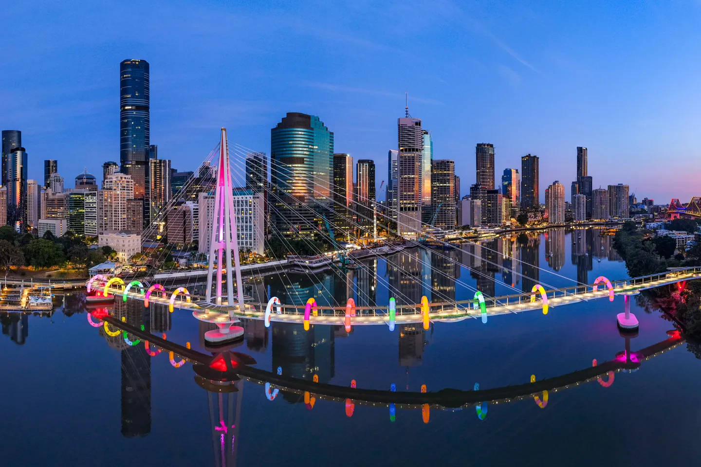 An aerial view of Brisbane city at dawn with Kangaroo Point Bridge lit up with rainbow arches of ANZ's Walk This Way by Craig Karl. 