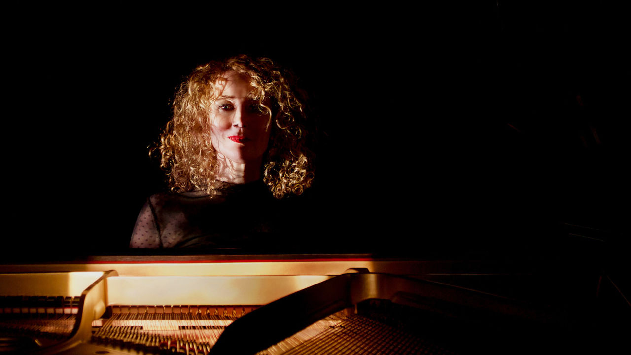 Gabriella Smart sitting behind a piano in a dark room. 