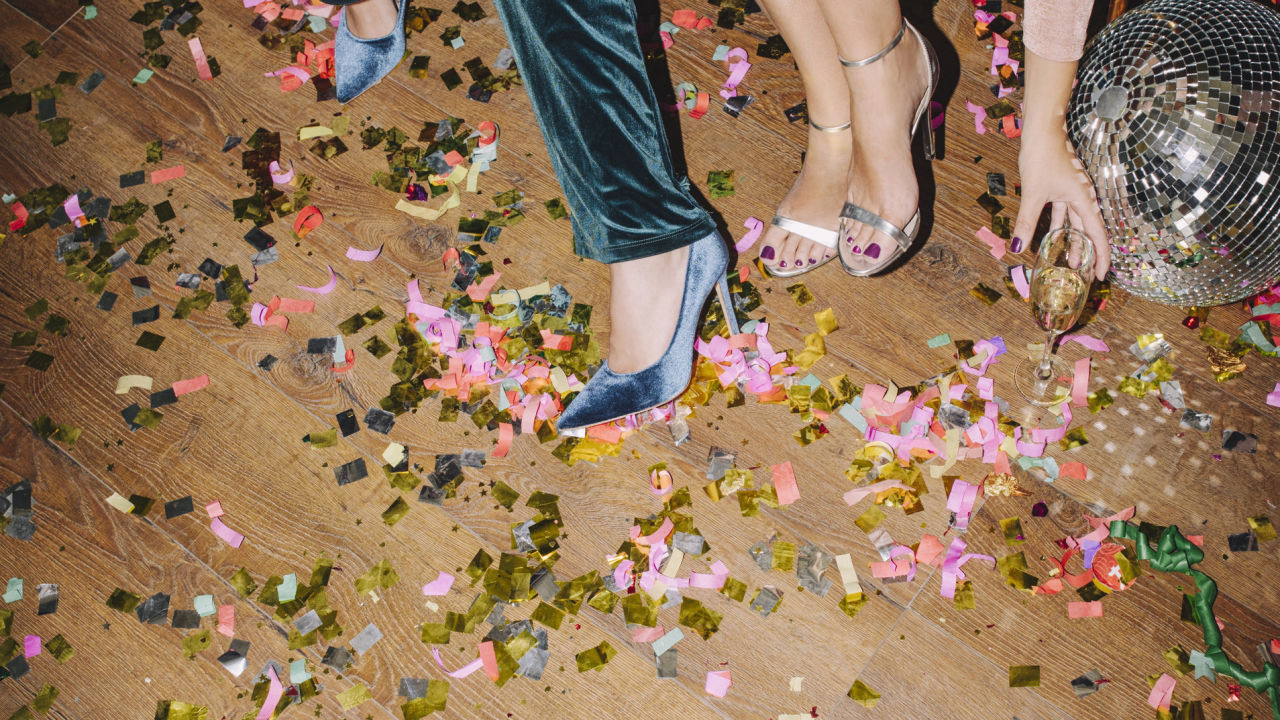 Party with confetti on the dancefloor, a disco ball and two people wearing heels. 