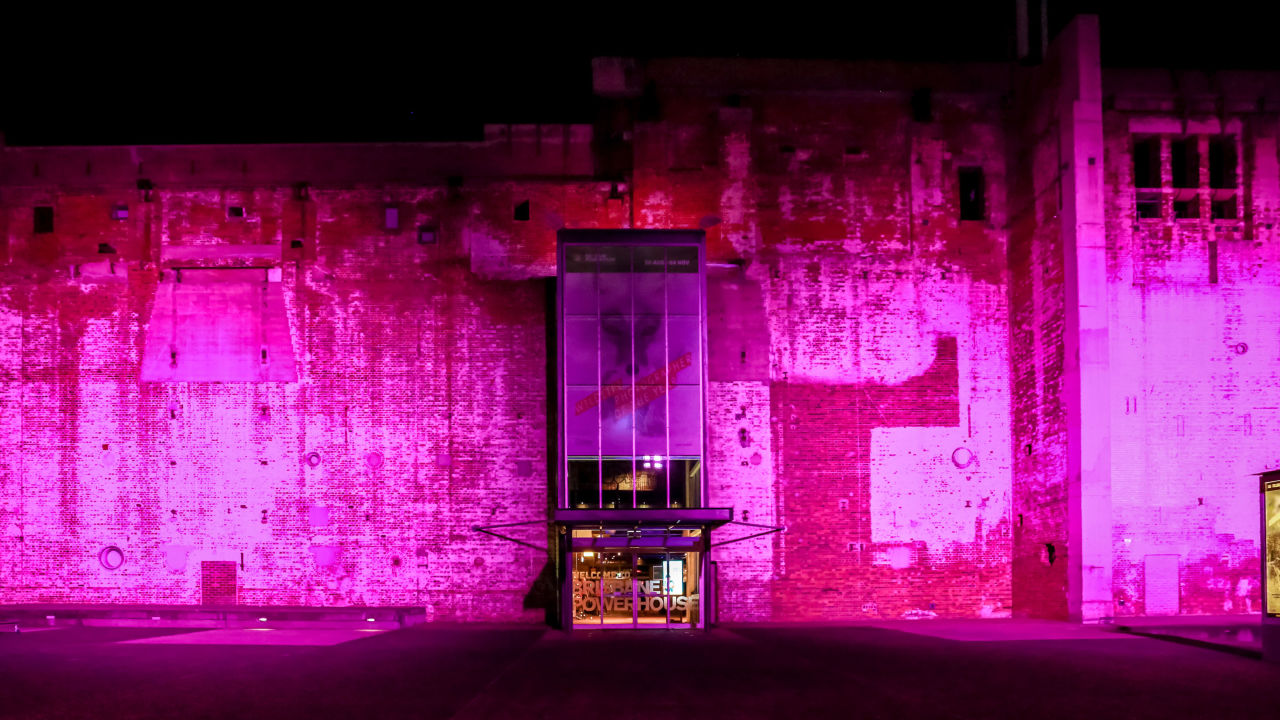 Brisbane Powerhouse's brick exterior wall lit up pink for Brisbane Festival. 