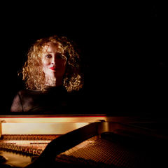Gabriella Smart sitting behind a piano in a dark room. 