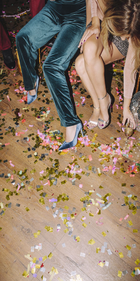 Party with confetti on the dancefloor, a disco ball and two people wearing heels. 
