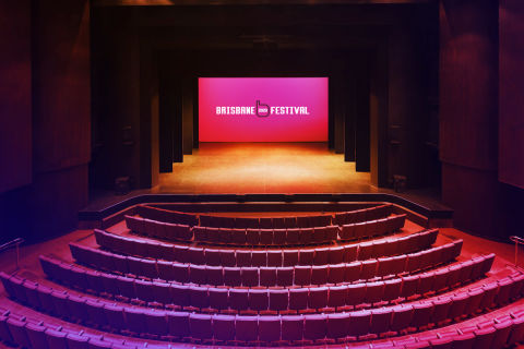 An empty theatre with the Brisbane Festival logo displayed on the stage screen.